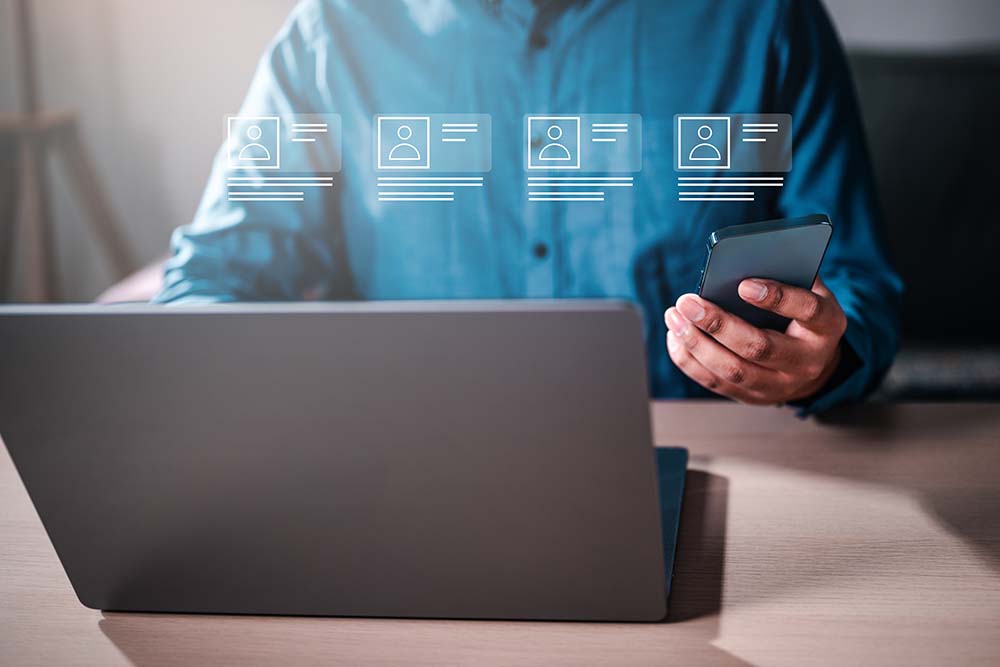 A man is sitting with a laptop and smartphone. shows a social media feed with multiple posts. mobile access control, 1# Toronto Security company, best security company Toronto, experienced security company toronto safelink group, P8MX+GC Brampton, Ontario