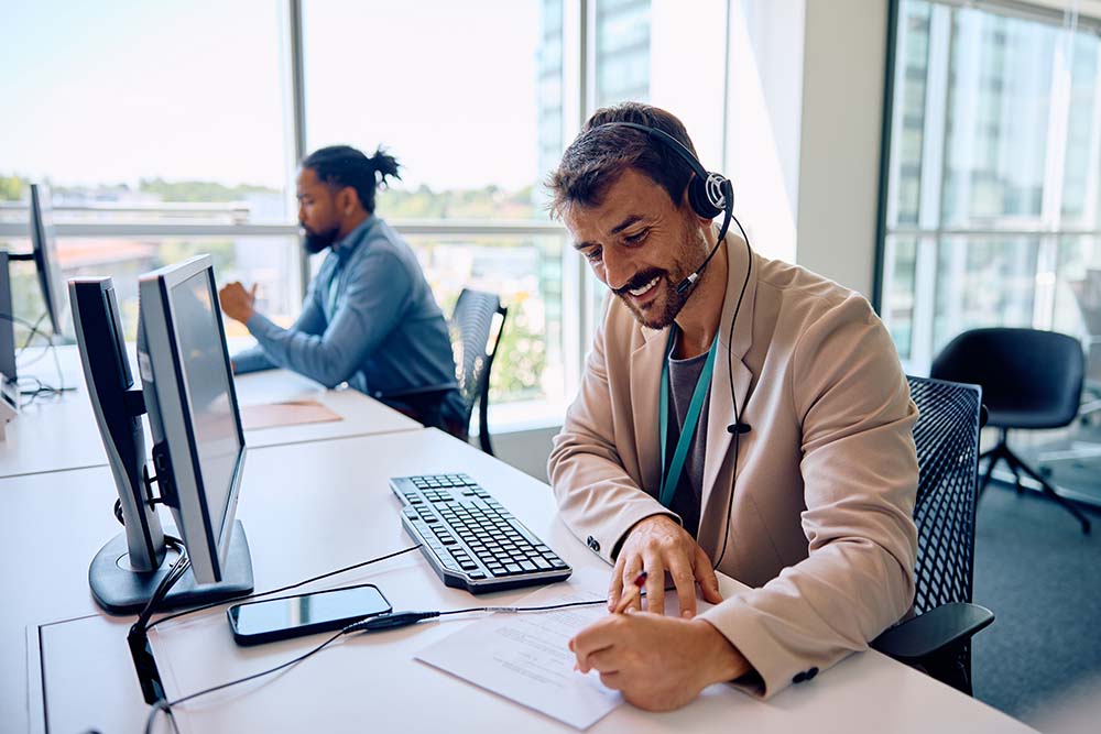 Happy call center agent taking notes while working on computer in office. managed it security safelink specialist is it solutions